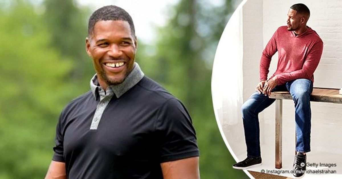 Michael Strahan Models His Own Clothing Line As He Poses In A Red Hoodie And Denim Pants 