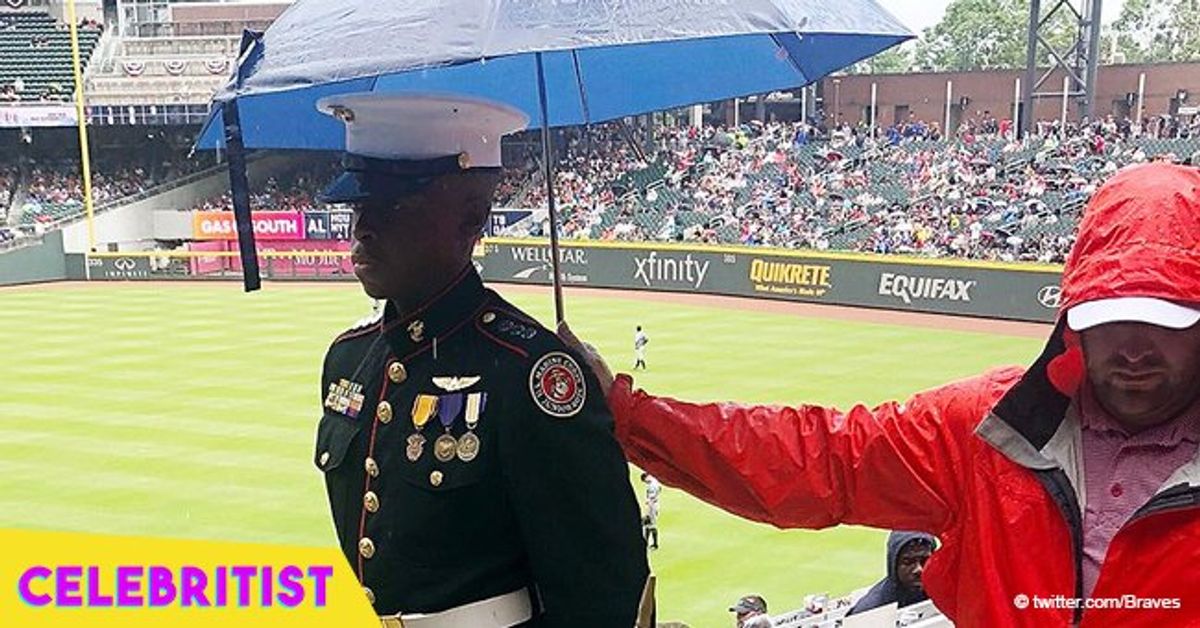 Photo of baseball fan holding umbrella over Marine Corps JROTC member